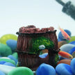 Decorative aquarium ornament with green moss and brown base, surrounded by colorful fish and stones.
