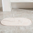 Oval-shaped bath mat on a marble floor with a glass of water nearby.