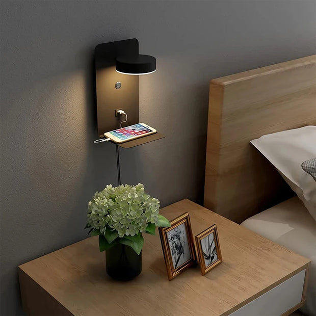 Wall-mounted lamp on a nightstand with a vase of flowers and photo frames in a bedroom setting.