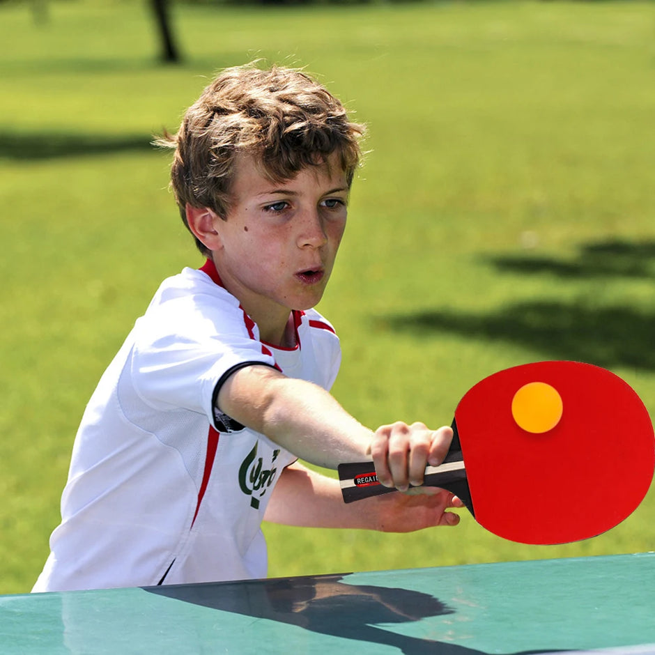 Young boy playing table tennis outdoors with a green background