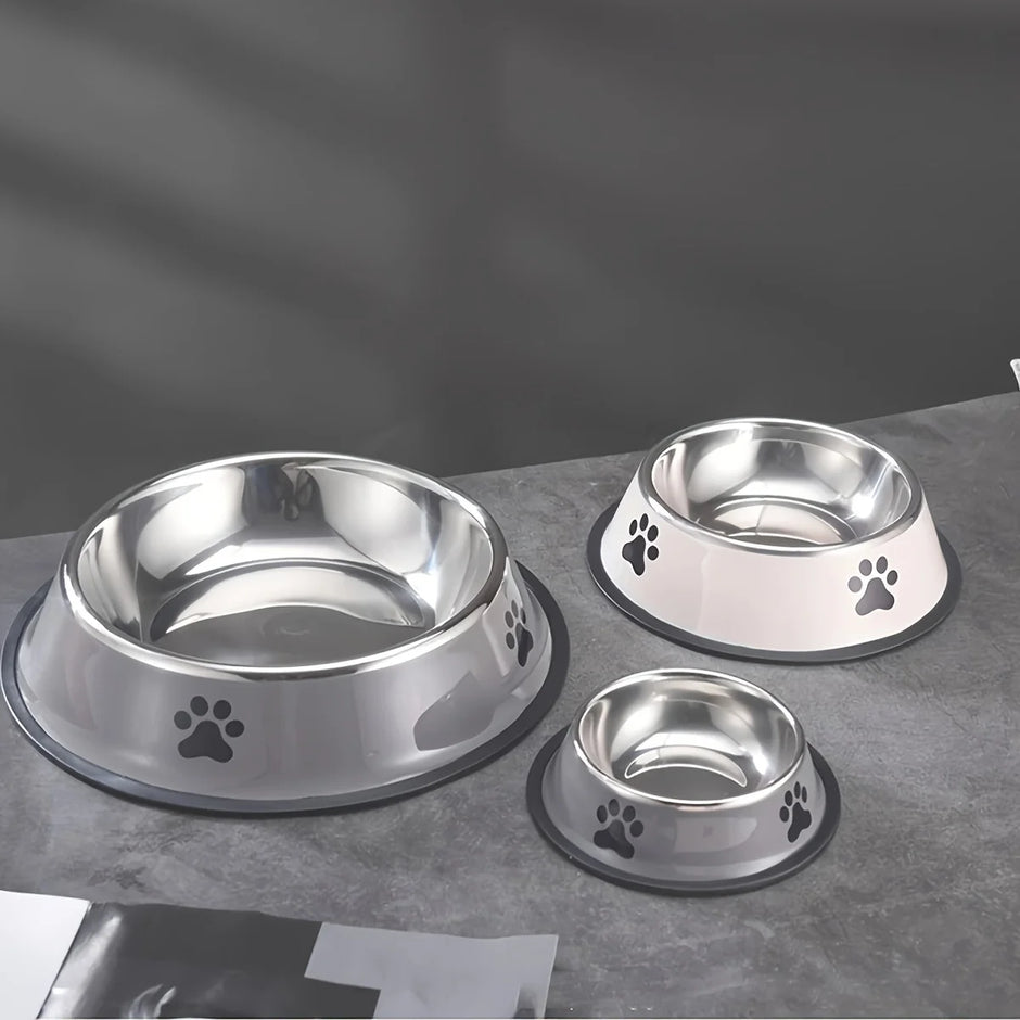 Set of three stainless steel pet bowls with paw prints on a gray surface