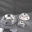 Set of three stainless steel pet bowls with paw prints on a gray surface