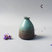 Teal ceramic vase on a light gray background with small purple flowers.