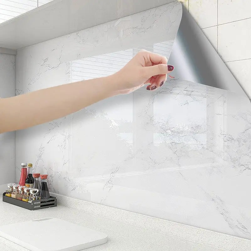 Person applying a marble-patterned adhesive vinyl sheet to a kitchen wall.