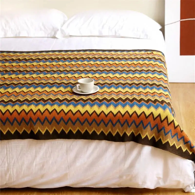 Colorful zigzag patterned blanket on a bed with a cup and saucer.