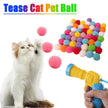 Cat playing with colorful teasing pet ball and a hand holding a launcher.