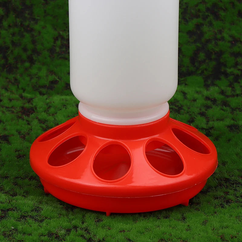 Red plastic chicken feeder with a white container on a green grass background