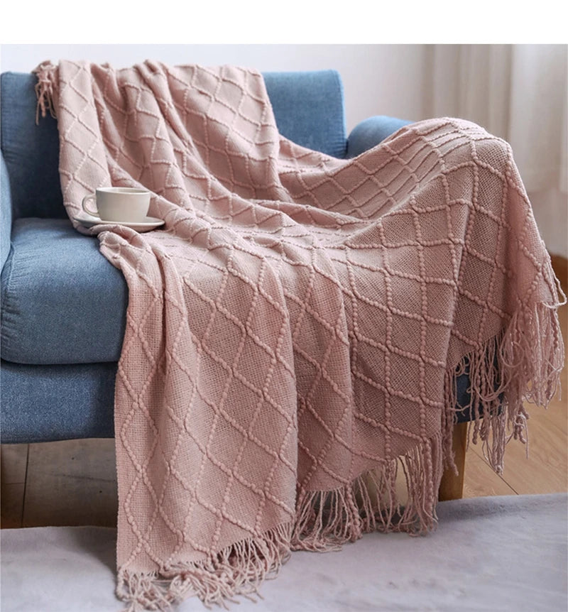 Pink textured throw blanket draped over a blue sofa with a white bowl on a wooden table.