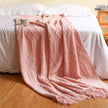 Pink textured blanket draped over a bed with a wooden headboard.