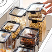 Set of clear food storage containers with black lids on a kitchen counter.