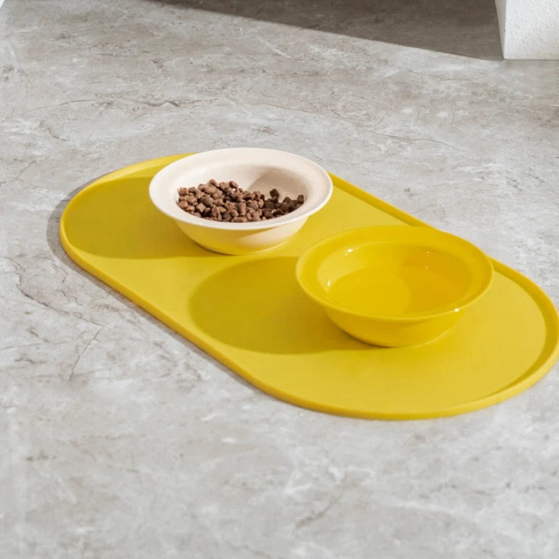 Yellow pet feeding mat with two bowls on a gray surface