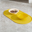 Yellow pet feeding mat with two bowls on a gray surface