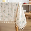 Floral patterned tablecloth with tassels on a wooden table.