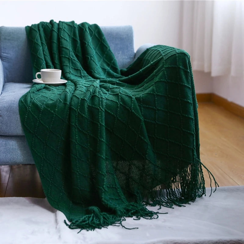 Green blanket draped over a sofa with a cup on a table.