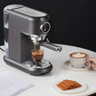Espresso machine making a shot of espresso on a white surface with a cup of coffee and cookies.