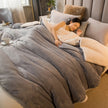 Woman lying on a bed with gray comforter and beige pillows, surrounded by cozy decor.