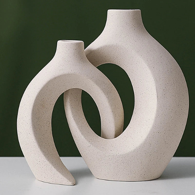 Two beige ceramic vases with a unique design on a white surface and green background