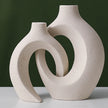 Two beige ceramic vases with a unique design on a white surface and green background