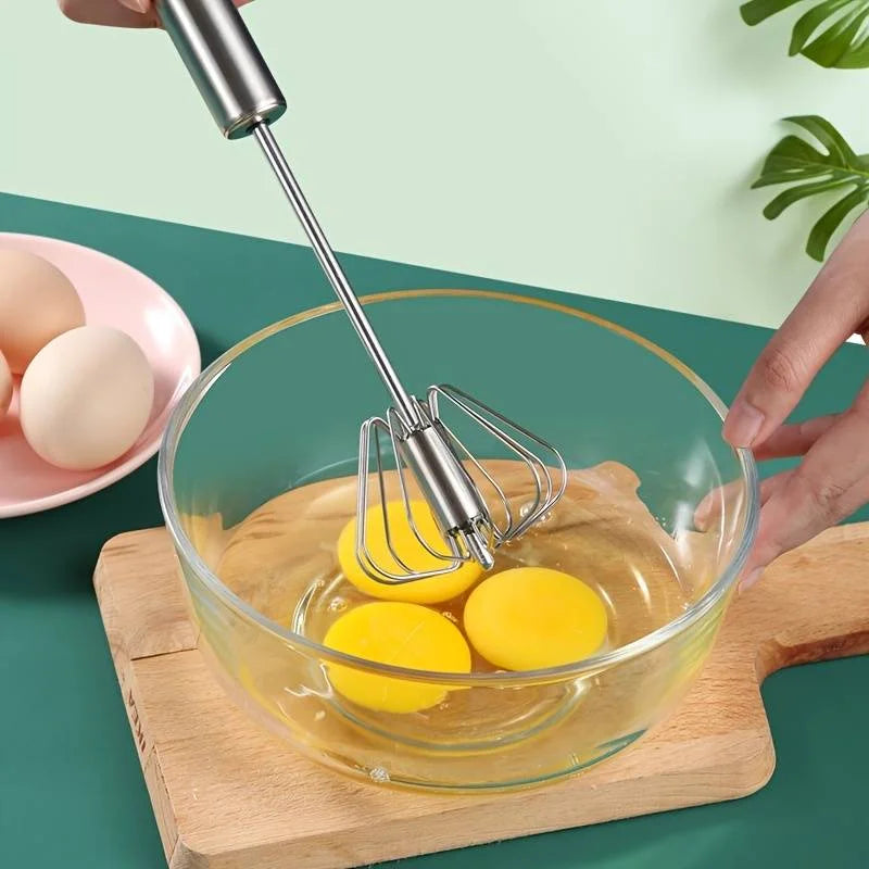 Person whisking eggs in a glass bowl with a hand mixer on a green surface.