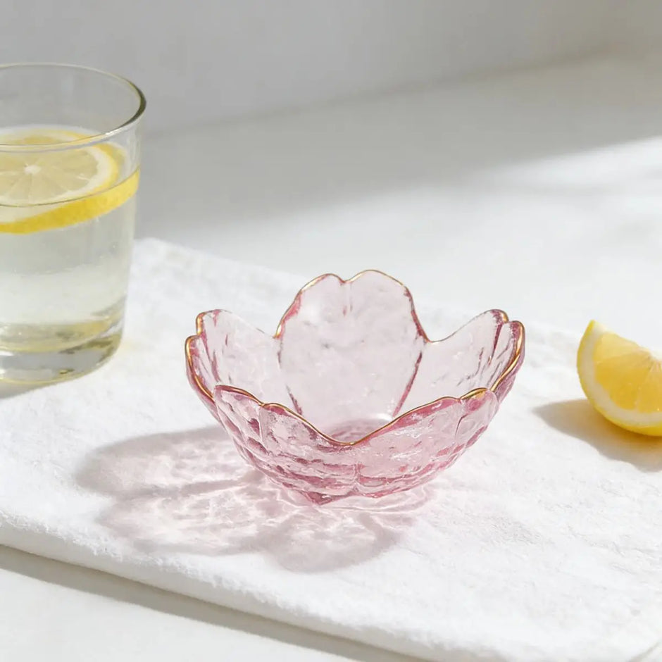 Pink glass bowl on a white surface with a glass of water and lemon slices.