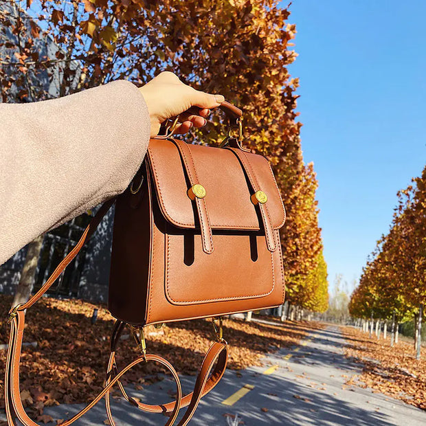 Brown leather handbag held by a person against an autumnal tree-lined street.