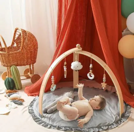 Baby playing on a mat with a wooden arch and hanging toys in a nursery.