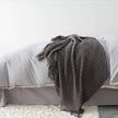 Gray textured blanket draped over a bed with white bedding.