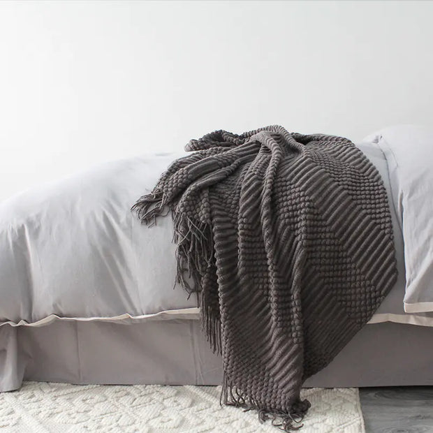 Gray textured blanket draped over a bed with white bedding.