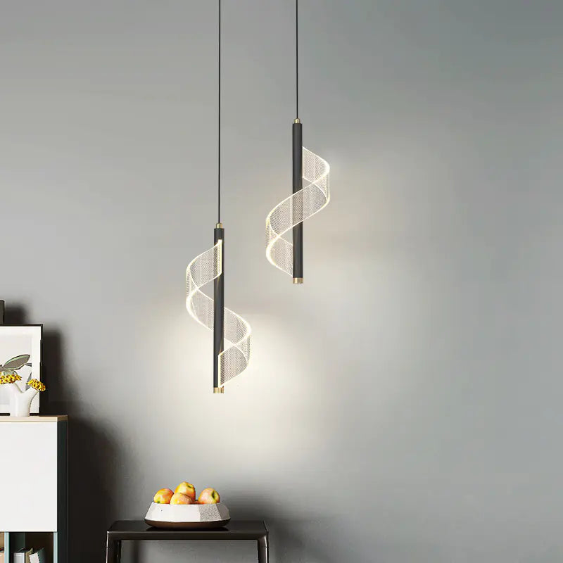 Two modern pendant lights hanging against a gray wall with a bowl of fruit on a table below.