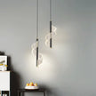 Two modern pendant lights hanging against a gray wall with a bowl of fruit on a table below.